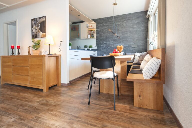 Home Staging für Ferienwohnung, Holzboden Rückwand mit grauer Granitverkleidung, Holzbank mit Tisch mit weiss grauen Kissen, Küche mit heller Arornfront und grauer Granitabdeckung.