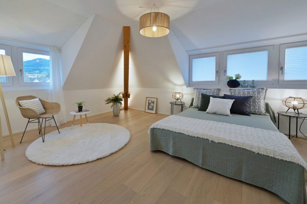 Möbiliertes Gästezimmer, Dachschräge Doppelbett, lindengrün weiss, anthrazit, recht Lesestuhl mit kleinem Tisch, Wände weiss, Boden Brauner Parkett.