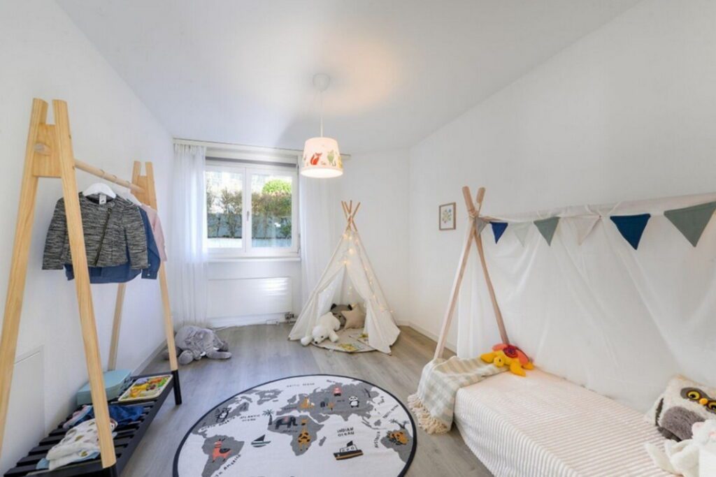 Leerstehende Immobilie, möbiliertes Kinderzimmer mit Babybett, Tipizelt und Kleiderstange mit Kleider, alles in helle Farben gehalten, mit vielen Stofftieren